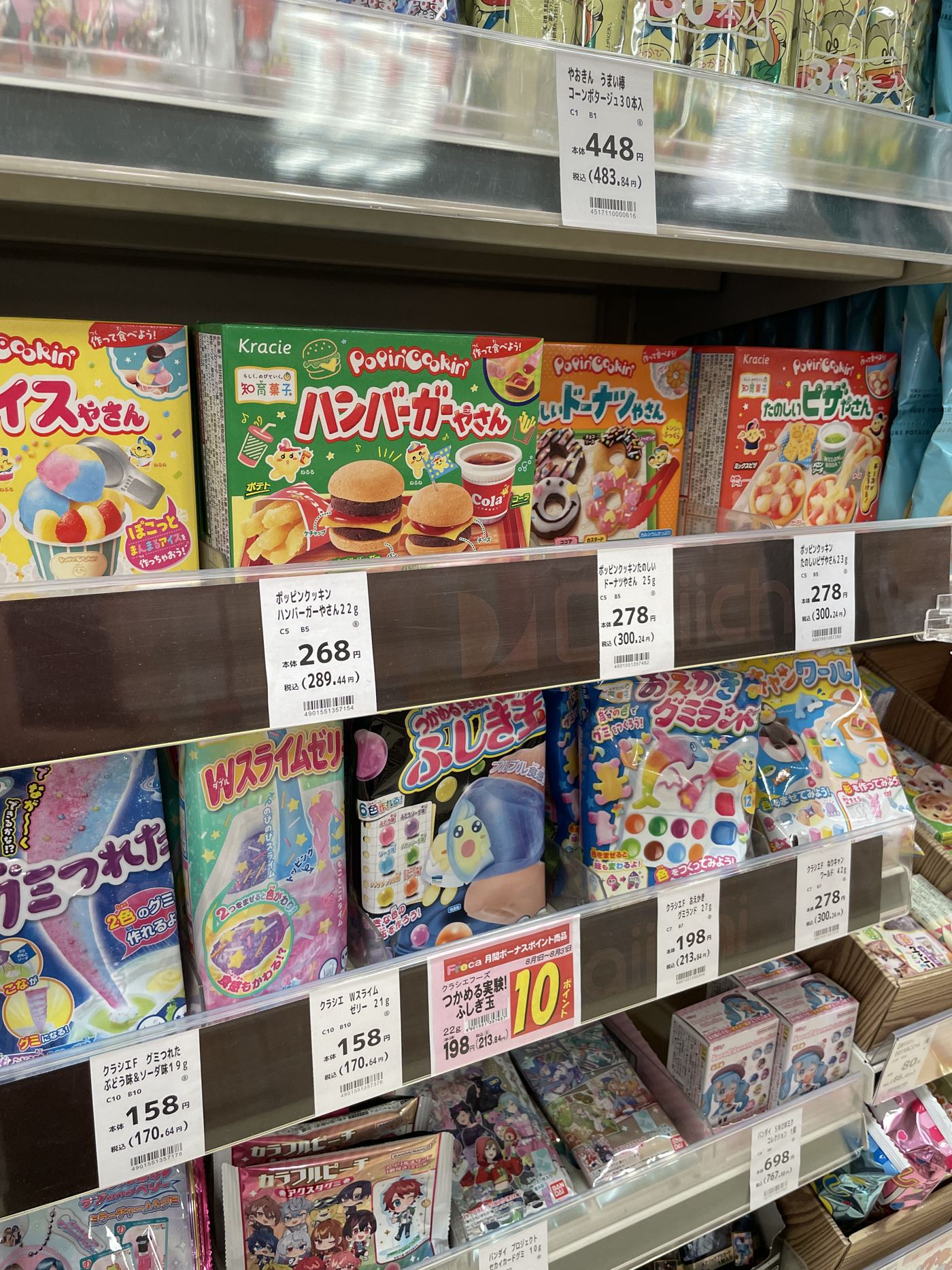A supermarket shelf in Japan stocked with DIY candy kits, with white paper price tags clipped along the shelf edge.