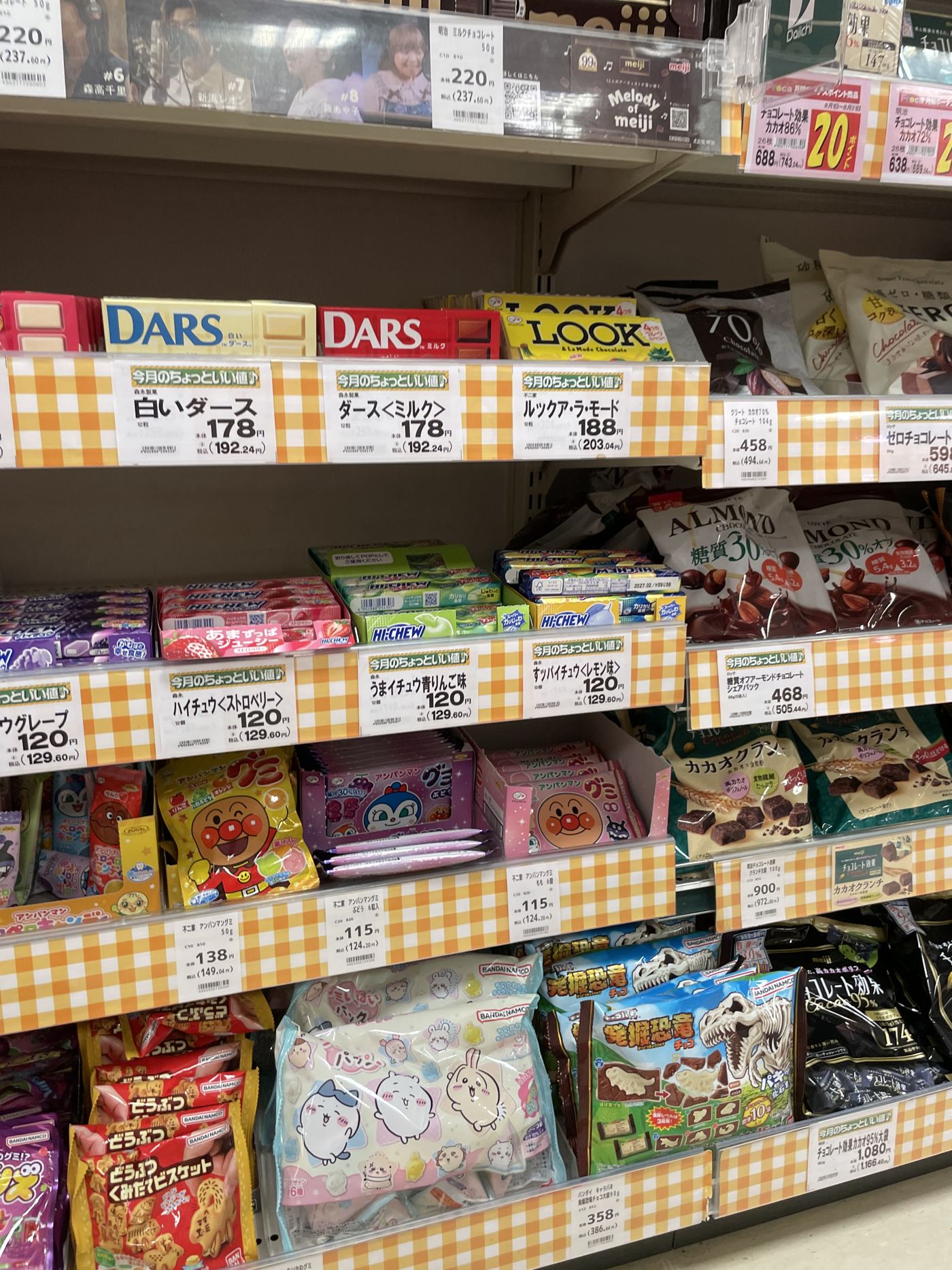 A Japanese supermarket chocolate and sweets aisle with orange-checked price tags along each shelf edge.